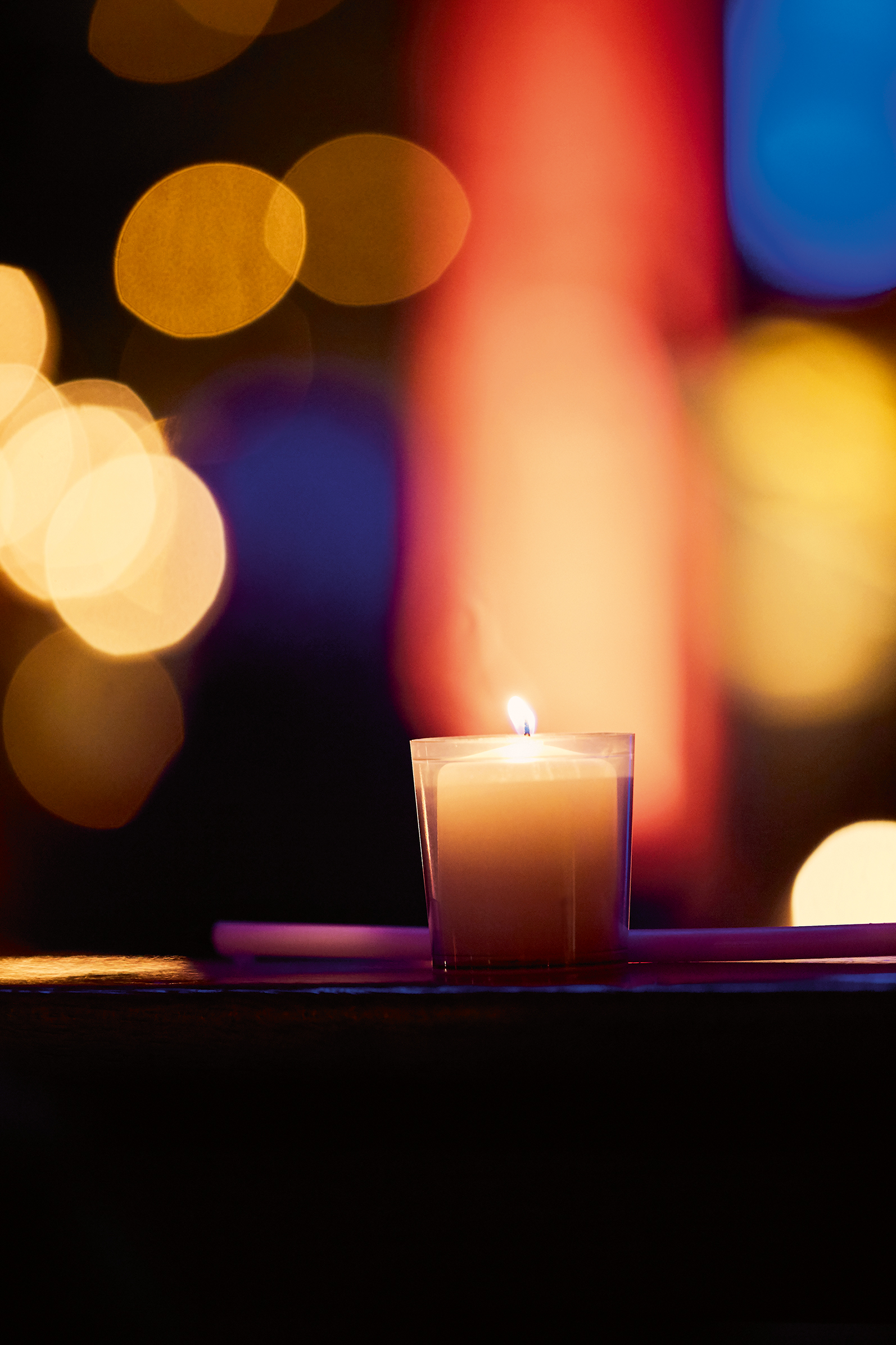 Eine Kerze im Pilgerkloster Werl. Im Hintergrund leuchten verschiedene Farben verschwommen. Eine Kerze im Pilgerkloster Werl. Im Hintergrund leuchten verschiedene Farben verschwommen.