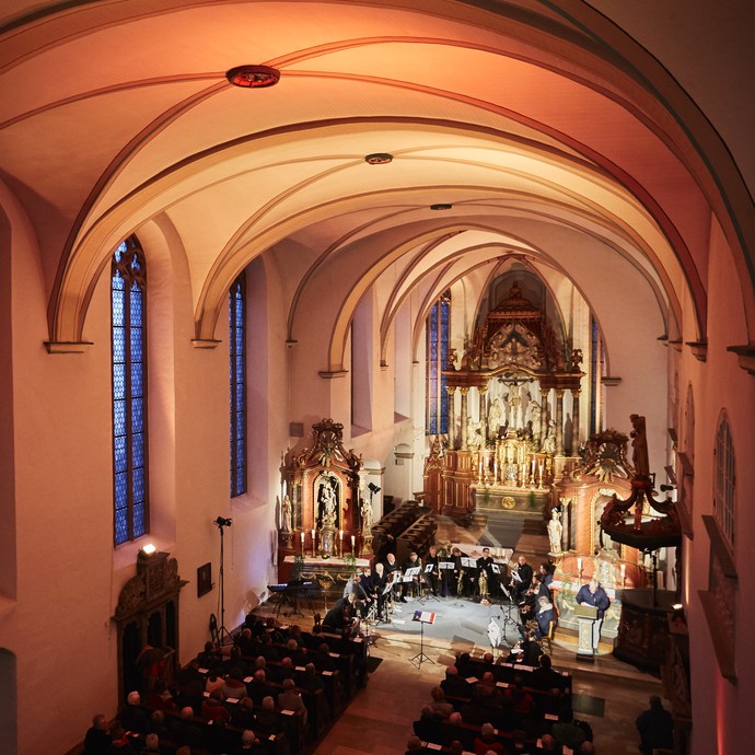 Die Kirche des ehemaliges Franziskanerkloster Warendorf von innen. Der Raum ist von warmem Licht ausgestrahlt. Zwischen den beiden Seitenaltären befinden sich Musikanten. Am rechten Seitenaltar befindet sich ein Ambo.© LWL Fotografie Sarah Bömer. Die Kirche des ehemaliges Franziskanerkloster Warendorf von innen. Der Raum ist von warmem Licht ausgestrahlt. Zwischen den beiden Seitenaltären befinden sich Musikanten. Am rechten Seitenaltar befindet sich ein Ambo.© LWL Fotografie Sarah Bömer.